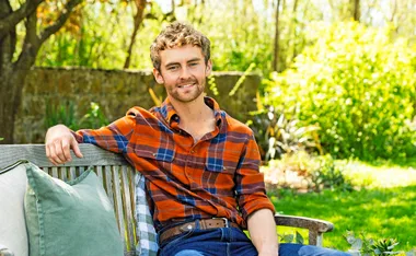 Farmer Jack, wearing a red checked shirt, sits in a garden on a bench.
