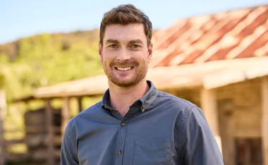 Farmer Thomas, wearing a blue shirt, stands in front of a rusty old building
