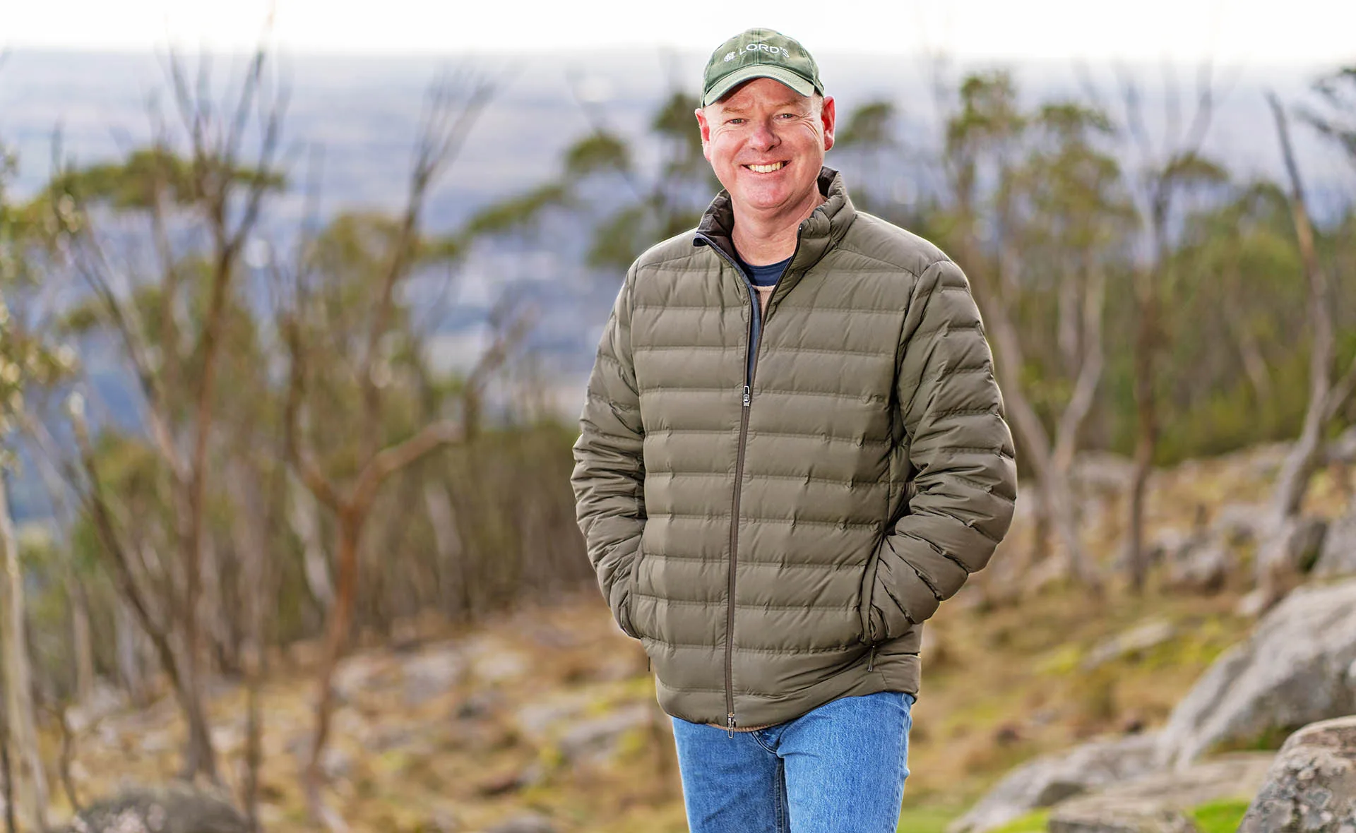 Tom Gleeson, his hands in the pocket of his jacket, stands in bushland.