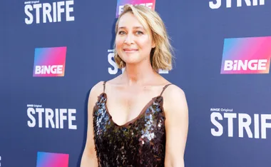 Asher Keddie poses in front of a Binge media wall in a maroon strap dress for the launch of Strife