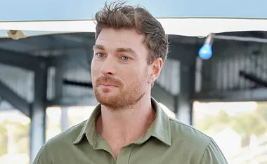 Farmer Thomas, wearing a khaki shirt, and standing on his farm, has an uncertain look on his face.