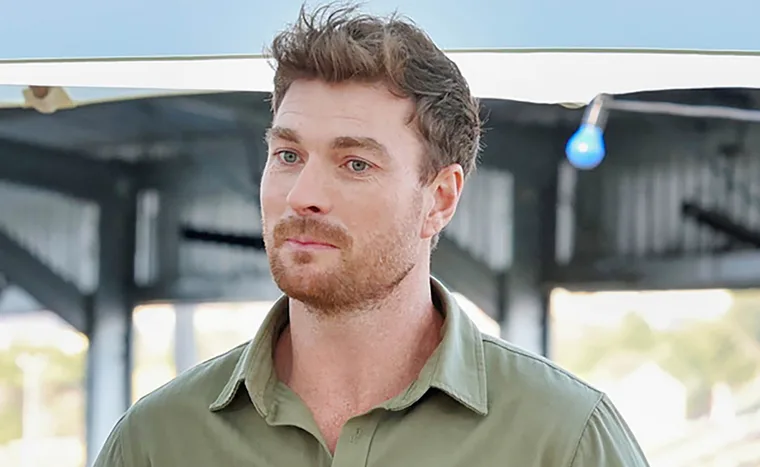 Farmer Thomas, wearing a khaki shirt, and standing on his farm, has an uncertain look on his face.