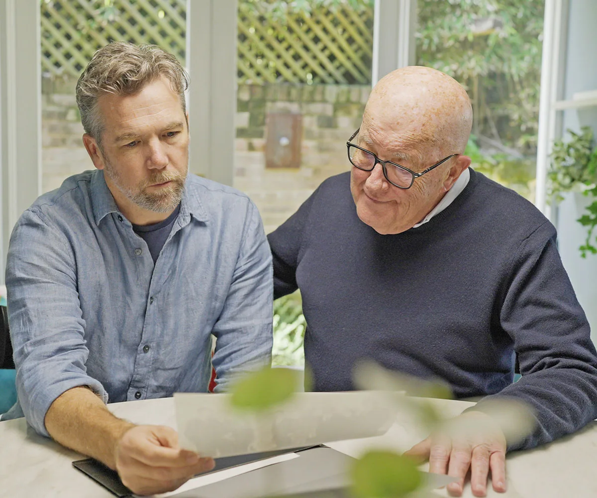 Patrick sits next to his uncle David, and the two of them look over documents together. 