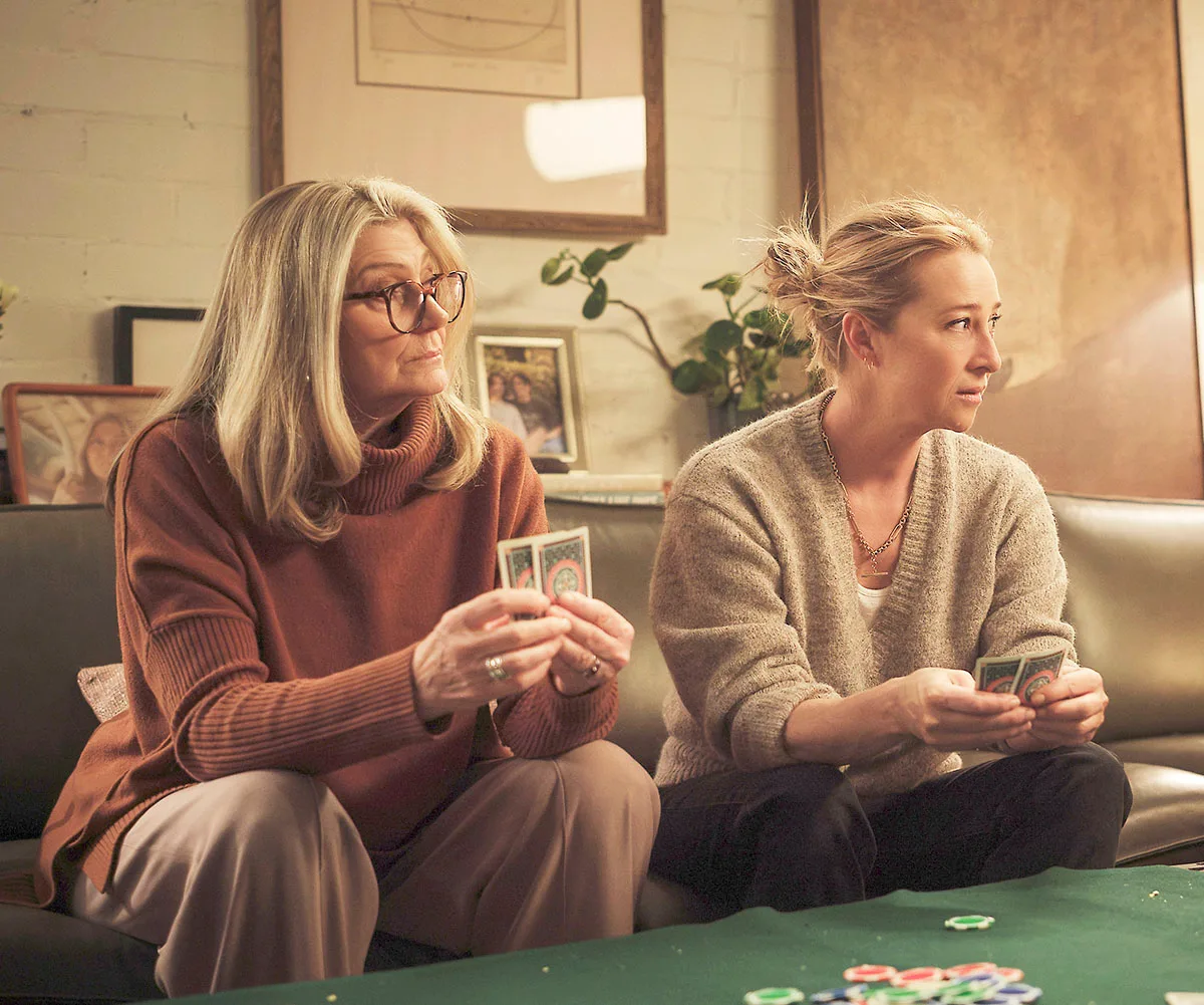 Tina Bursill and Asher Keddie sitting on a couch playing cards while filming a scene for Strife