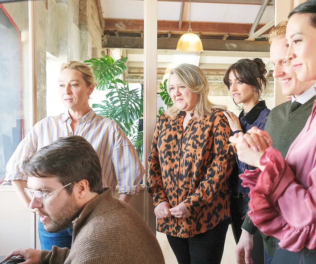 Eve and her team in a workplace all staring excitedly at a computer
