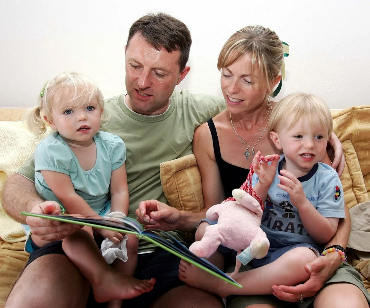 A picture of a man and woman sitting with two very young children reading a book.