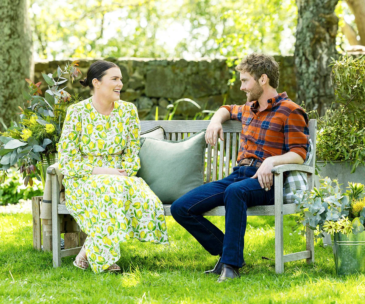 Jack sits on a bench in a garden alongside Chelsea, who is wearing a long floral dress.
