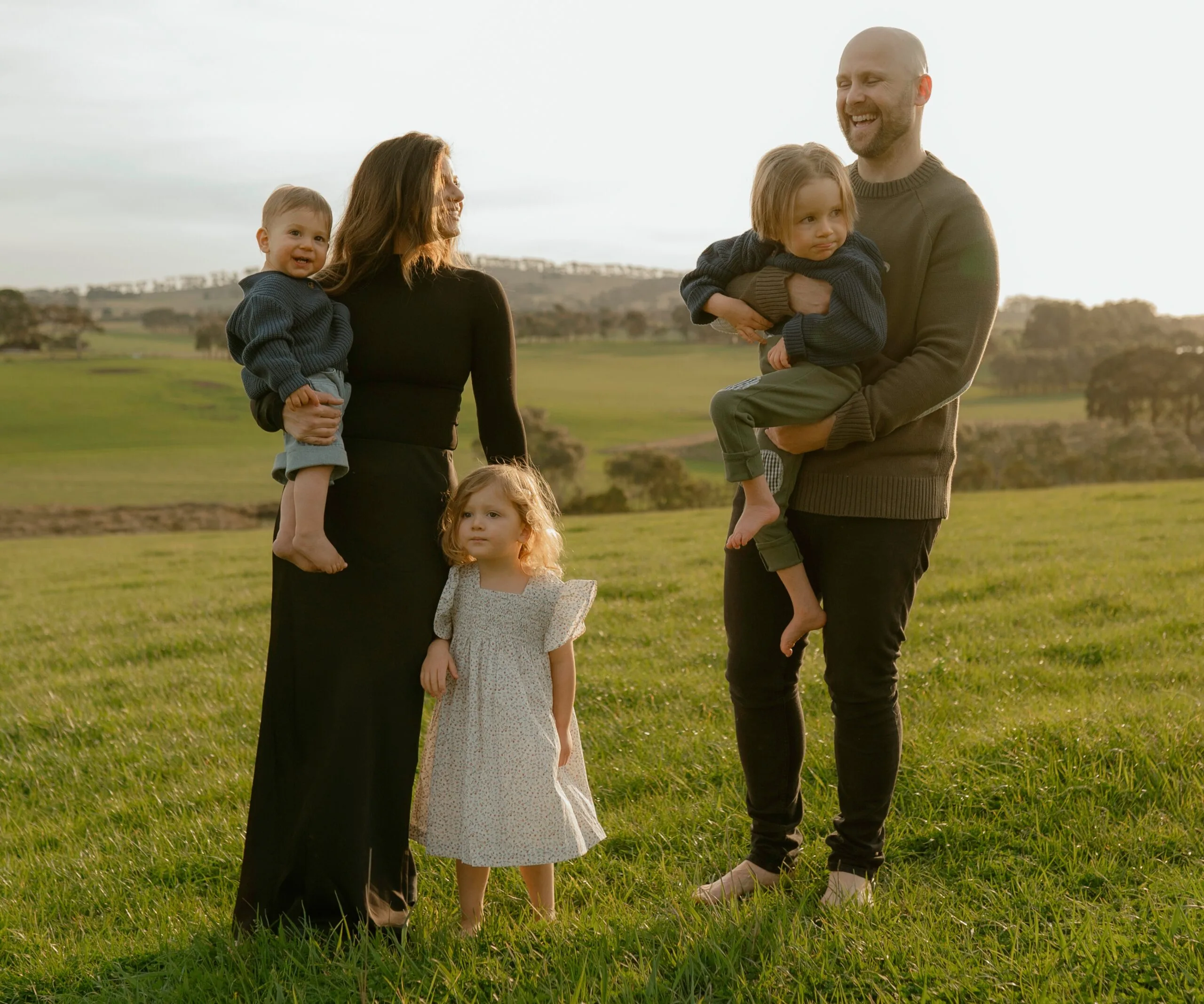 A man and woman stand on grass with their three children.