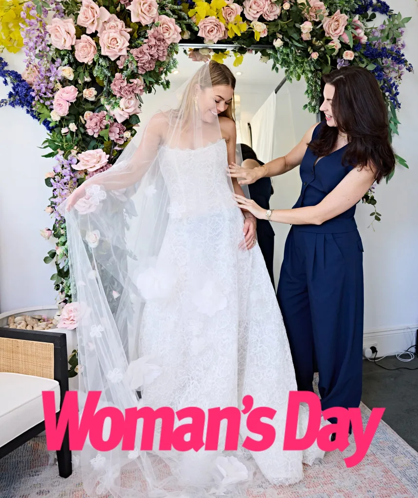 Jacqui stands with wedding dress designer Moira Rose in front of a mirror filled with flowers.