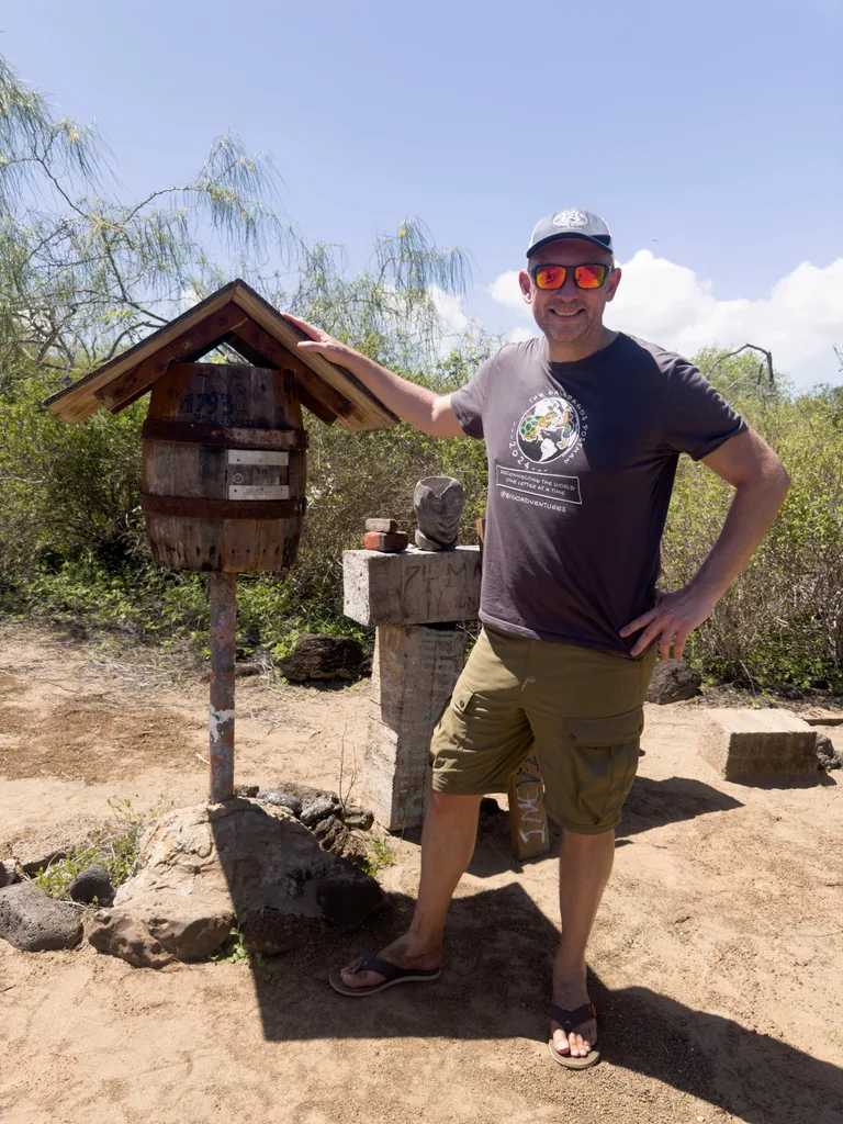 Jon Beardmore at the Galapagos postbox, which looks like a little barrel with a roof shading it.
