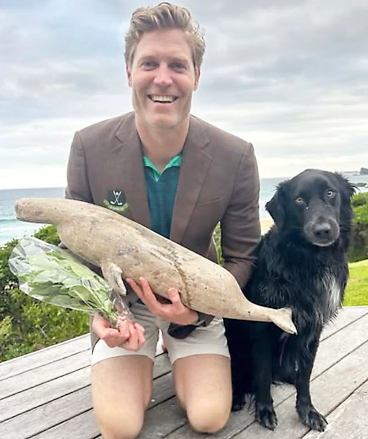 Dr Chris poses, kneeling, with his black labrador, Buzz, outdoors. 