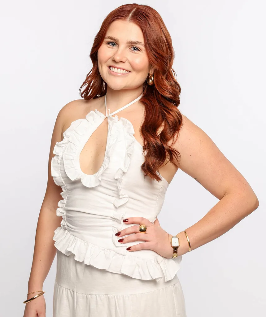 Bri, wearing a white frilly outfit, faces the camera with one hand on her hip.