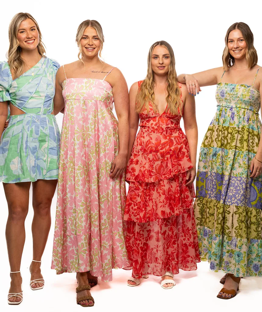 Four women in dresses stand facing the camera and smiling,