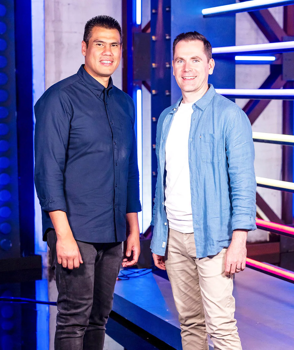 On left: Henry smiling in a navy button up and black pants. 
On right: Cade smiling in white t-shirt, open denim long sleeve shirt and beige pants on the LM set.