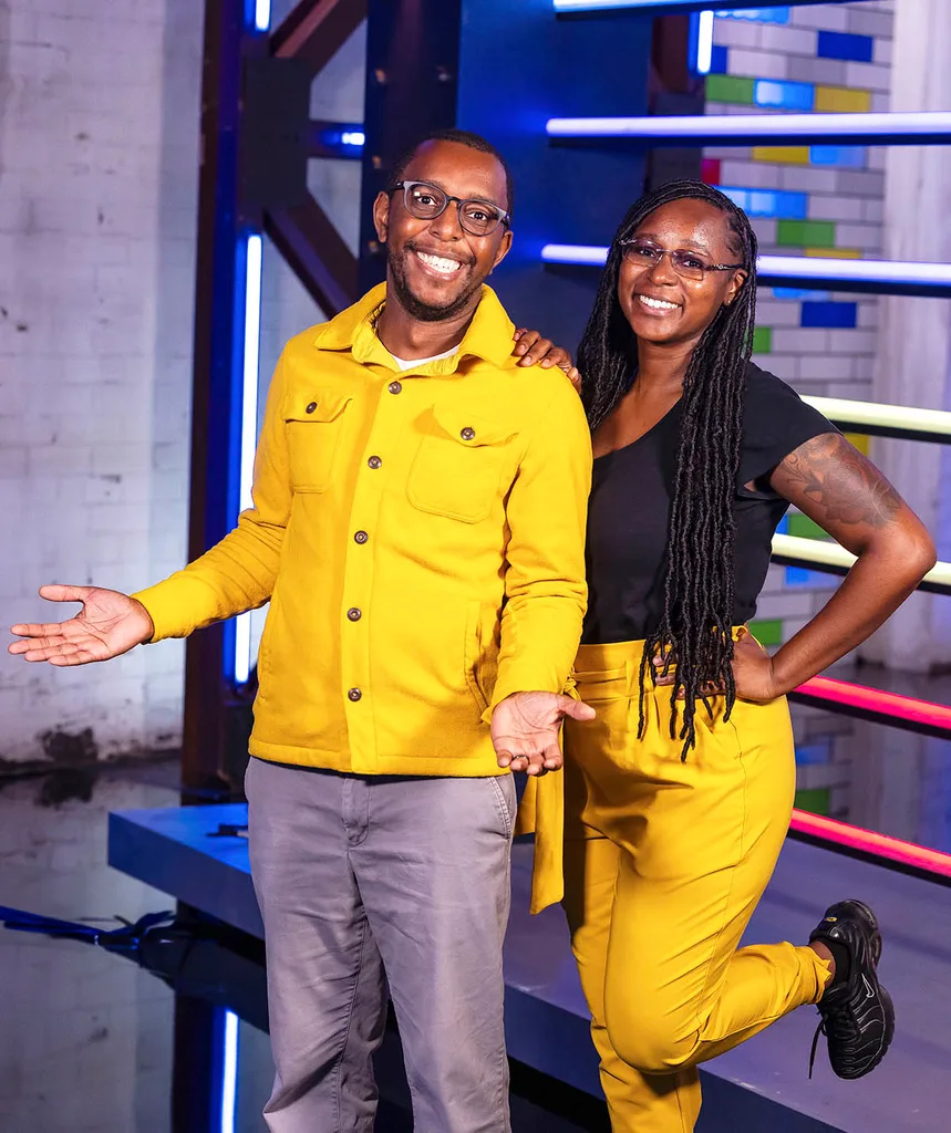 On left: Paul smiling with his hands out wearing glasses, a yellow jacket and grey pants. On right: His sister Nealita with long black dreaded hair, glasses, black t-shirt and yellow pants, hand on hip smiling. On set of LM.