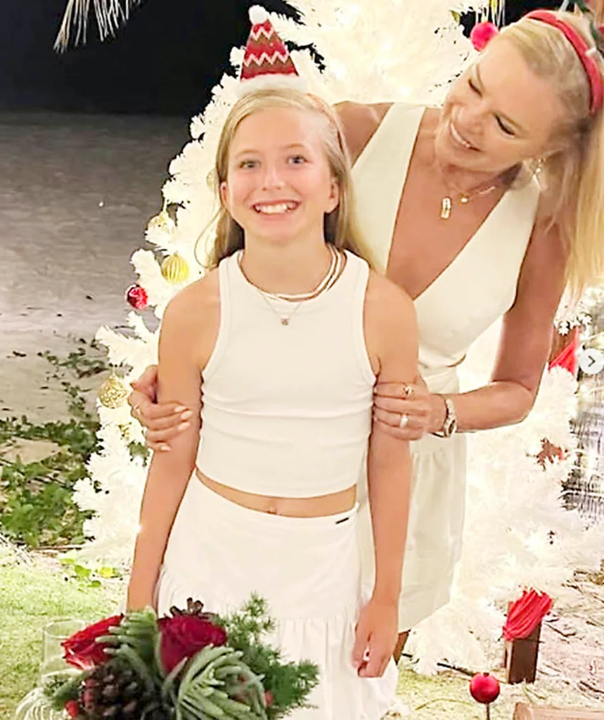 Sonia Kruger stands behind her daughter Maggie, looking down at her with a smile on her face. Both are wearing white and there is a white Christmas tree behind them.