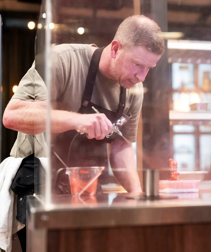 Tim is holding a spray gun looking stressed as he cooks in one of the hardest pressure tests
