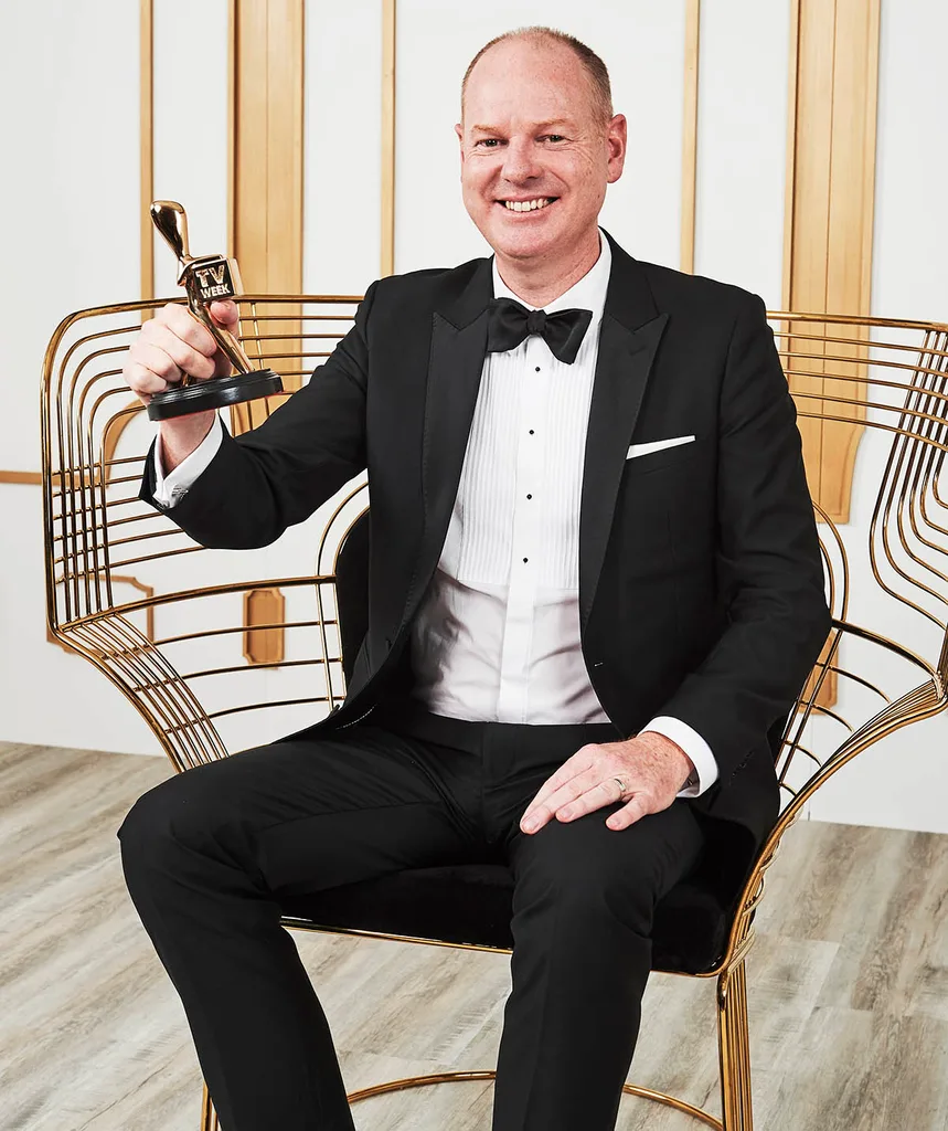 Tom Gleeson sits in a chair holding his Gold Logie in his hand.