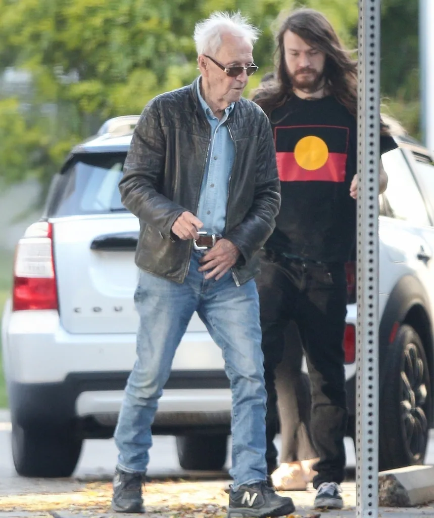 An older and younger man stand together on a street.