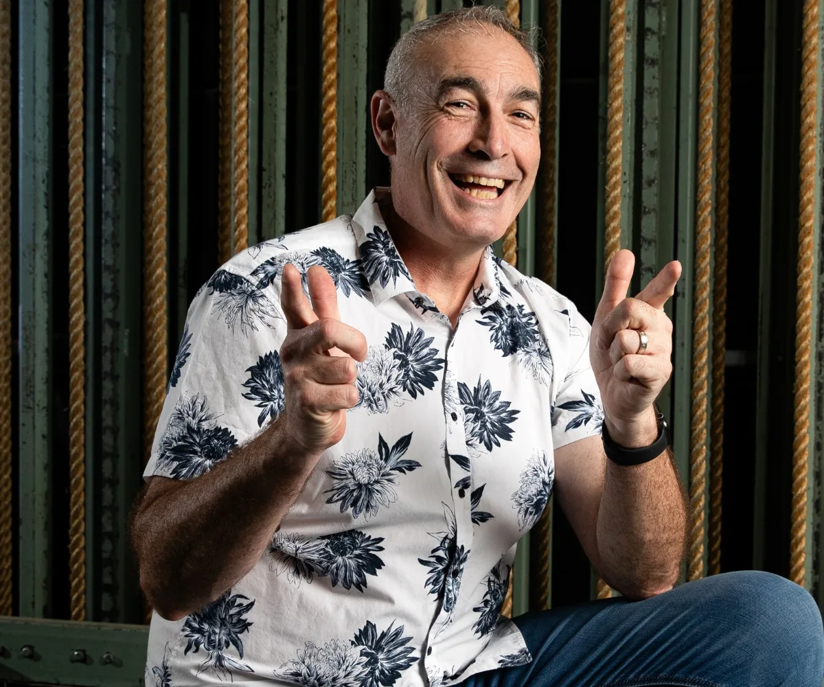 A man smiles at the camera and is pointing his fingers.