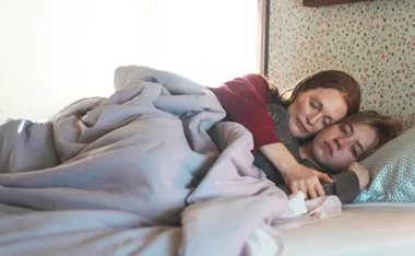 Julianne Moore and Sydney Sweeney lie in bed. Julianne has her arm around Sydney.