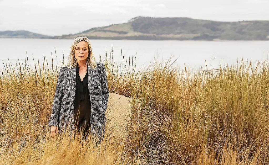 Marta stands, surrounded by grasses, with the ocean and mountains in the background.