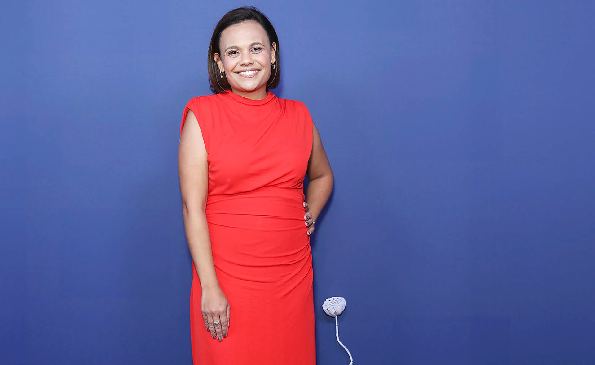 Miranda, in a red dress, poses for photographers in front of a blue background.