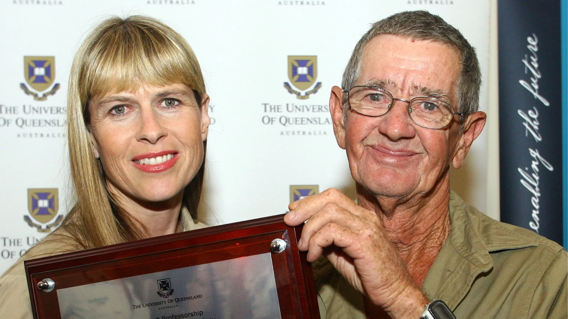 A blonde woman and older man stand together.