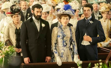 Two men in suits beside a woman dressed in a beautiful gown with an old fashioned hat.