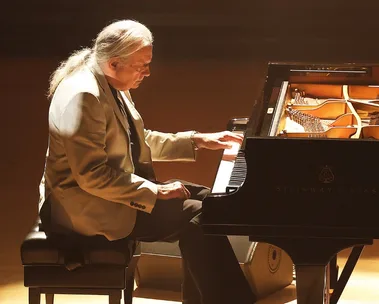 A man plays piano and there is an inset of the same man and woman smiling.
