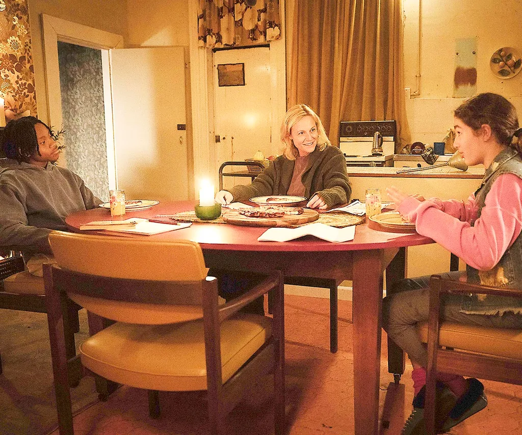 Marta, playing Stella, sitting at a kitchen table with her on-screen children, Otis and Iris.
