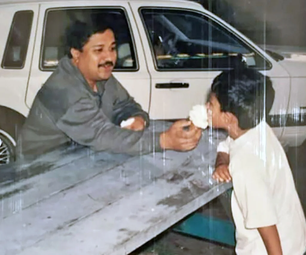 Darrsh's dad (left) in a grey jacket feeding his son, a young Darrsh, an ice-cream across the table pictured in a white t-shirt