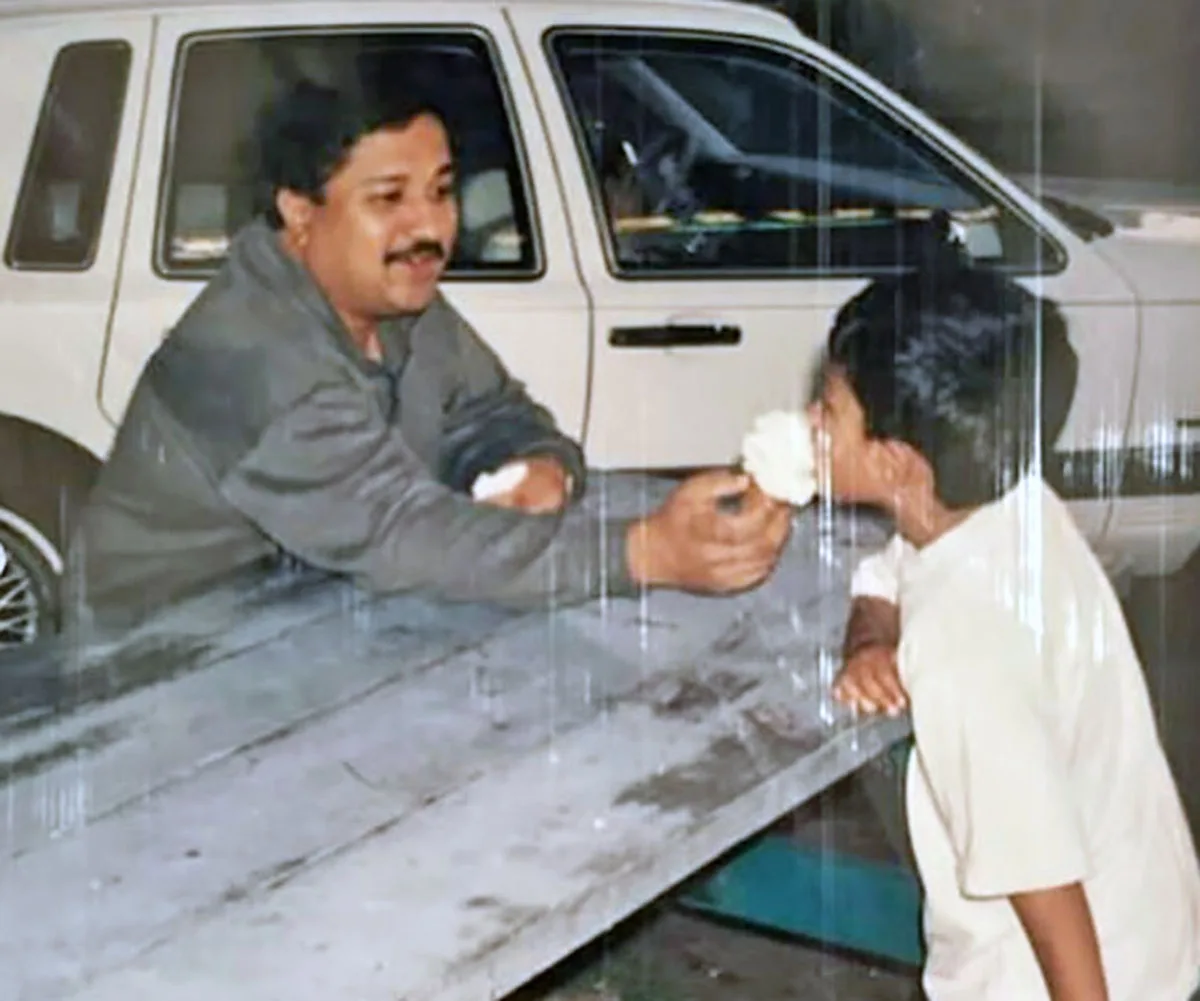Darrsh's dad (left) in a grey jacket feeding his son, a young Darrsh, an ice-cream across the table pictured in a white t-shirt