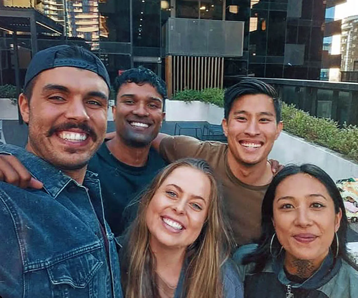 The group are pictured smiling and taking a selfie in front of an apartment block