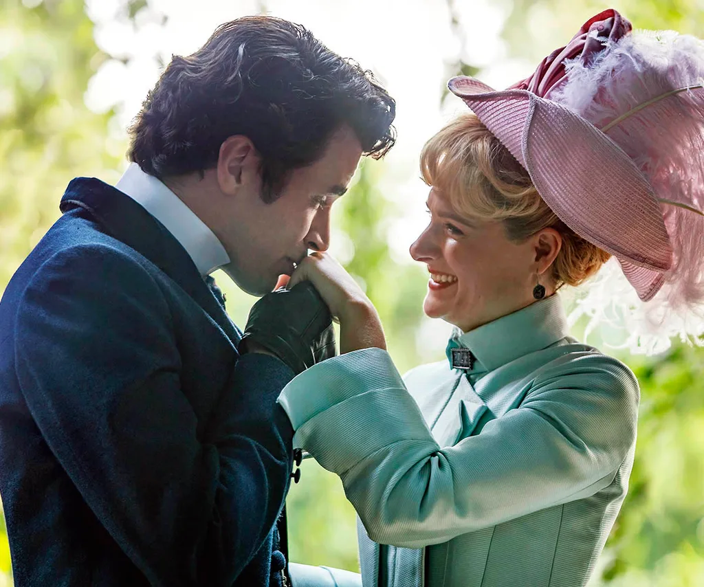 Larry kisses Marian's hand. She is wearing a pink hat and aqua dress and he is in a suit. Green leaves in the background.