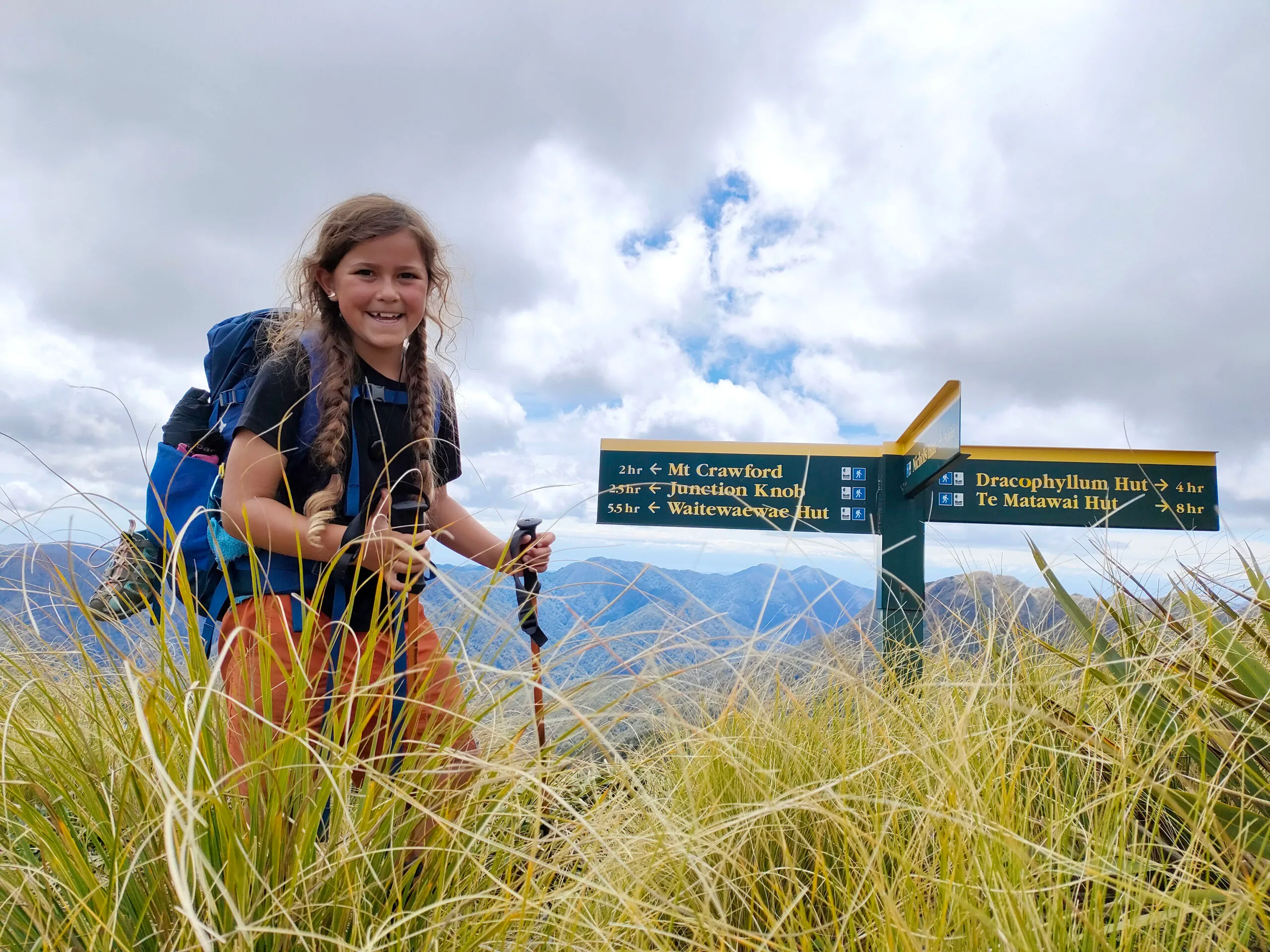 Emilie all smiles reaching the turn-off to the solid wooden shelter of Nichols Hut after several hard yards of tramping, climbing and slipping and sliding along the Main Ridge route. (Image: Supplied)