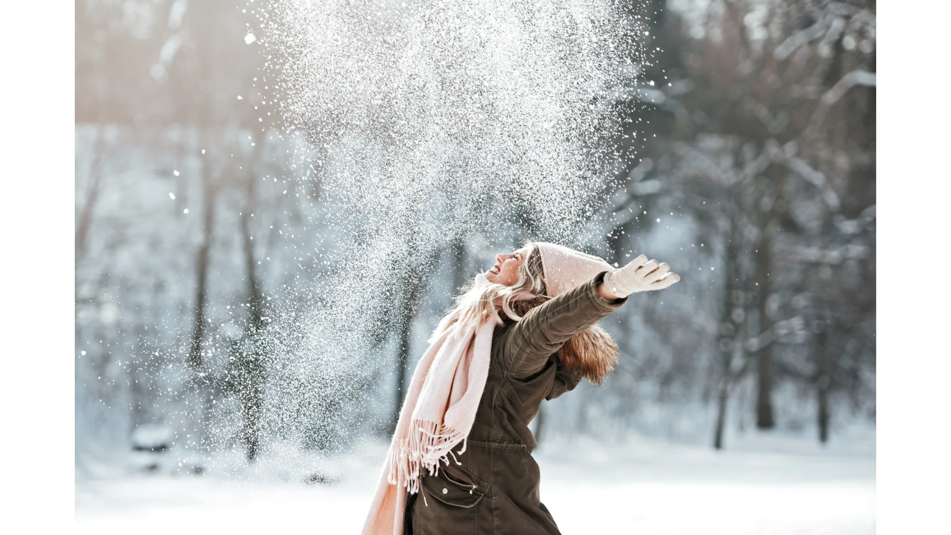 An elated woman throws her arms up in the snow.