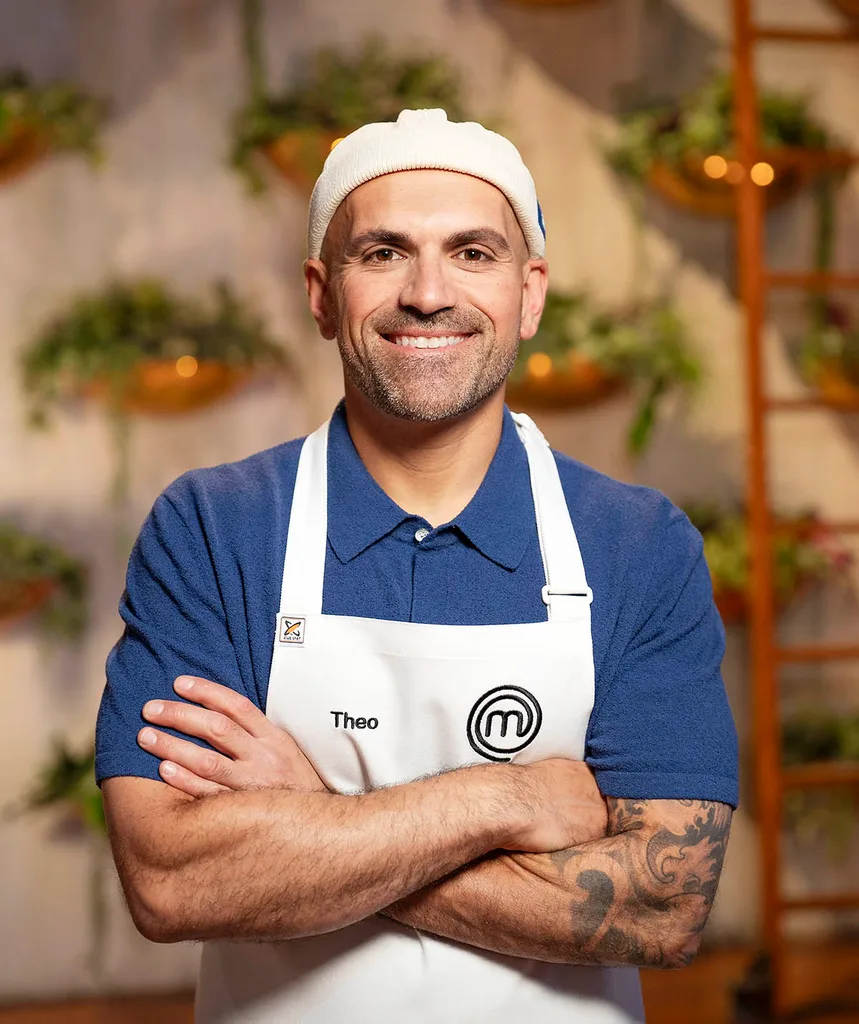 Theo is smiling with his arms crossed in a promo pic for MasterChef while wearing a blue polo shirt, white apron and white backwards cap