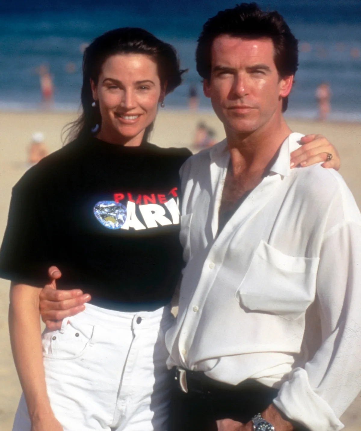 A young Keely and Pierce stand on the beach.