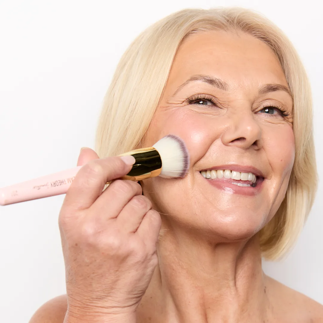 Smiling woman applying makeup with a makeup brush