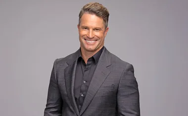 Denham Hitchcock, wearing a grey suit, poses in front of a grey background, smiling.