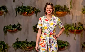 MasterChef judge Sofia Levin, wearing a colourful dress, stands in front of some plants, with a hand on her hip, smiling.