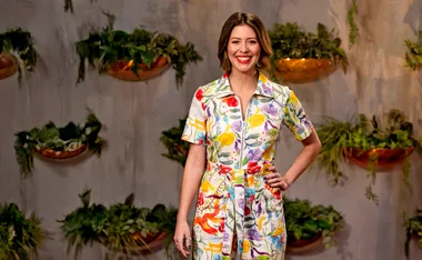 MasterChef judge Sofia Levin, wearing a colourful dress, stands in front of some plants, with a hand on her hip, smiling.