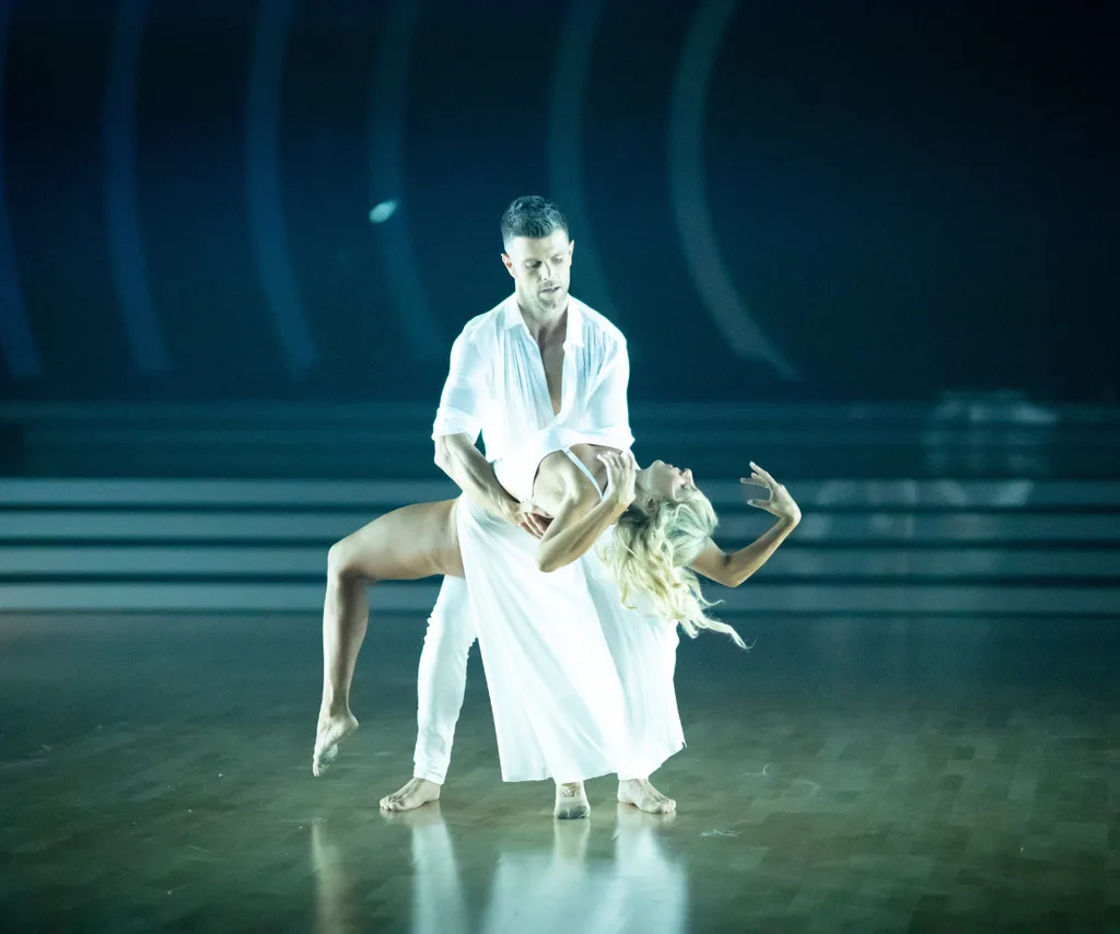 Trent and Jess, both dressed in white, dance on a darkened dance floor on Dancing With The Stars