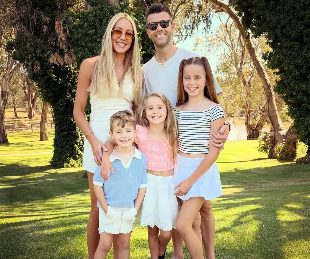 Trent with wife Brooke, daughters Harper and Mackenzie, and son Parker, stand in a group, against a backdrop of grass and trees.