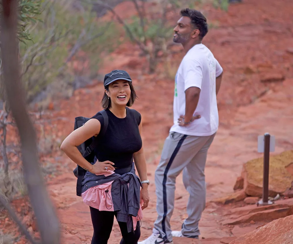 Melissa Leong and Nazeem Hussain, both wearing walking gear, pose in central Australia, Melissa smiling and Nazeem looking into the distance.