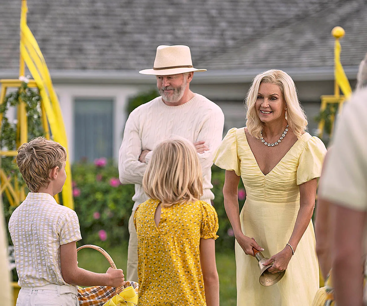 Harris and Tipper are smiling out the frnt of their beautiful home while talking to a little boy and girl. They are all dressed in yellows and whites.