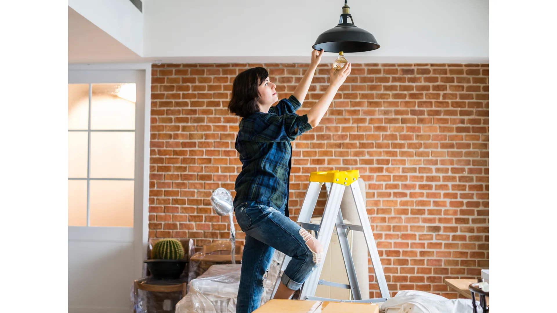 A woman on a ladder replaces a lightbulb.