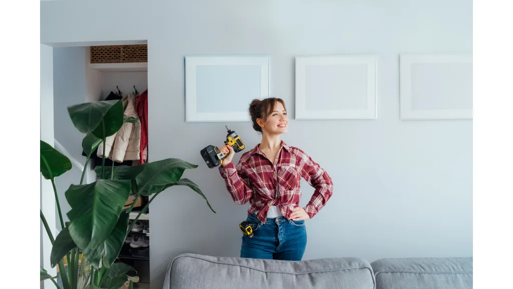 A woman dressed in a flannel shirt looks proud of herself as she holds a power drill.
