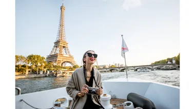 A woman laughs while holding a camera and sailing down the Seine River in front of the Eiffel Tower in Paris.